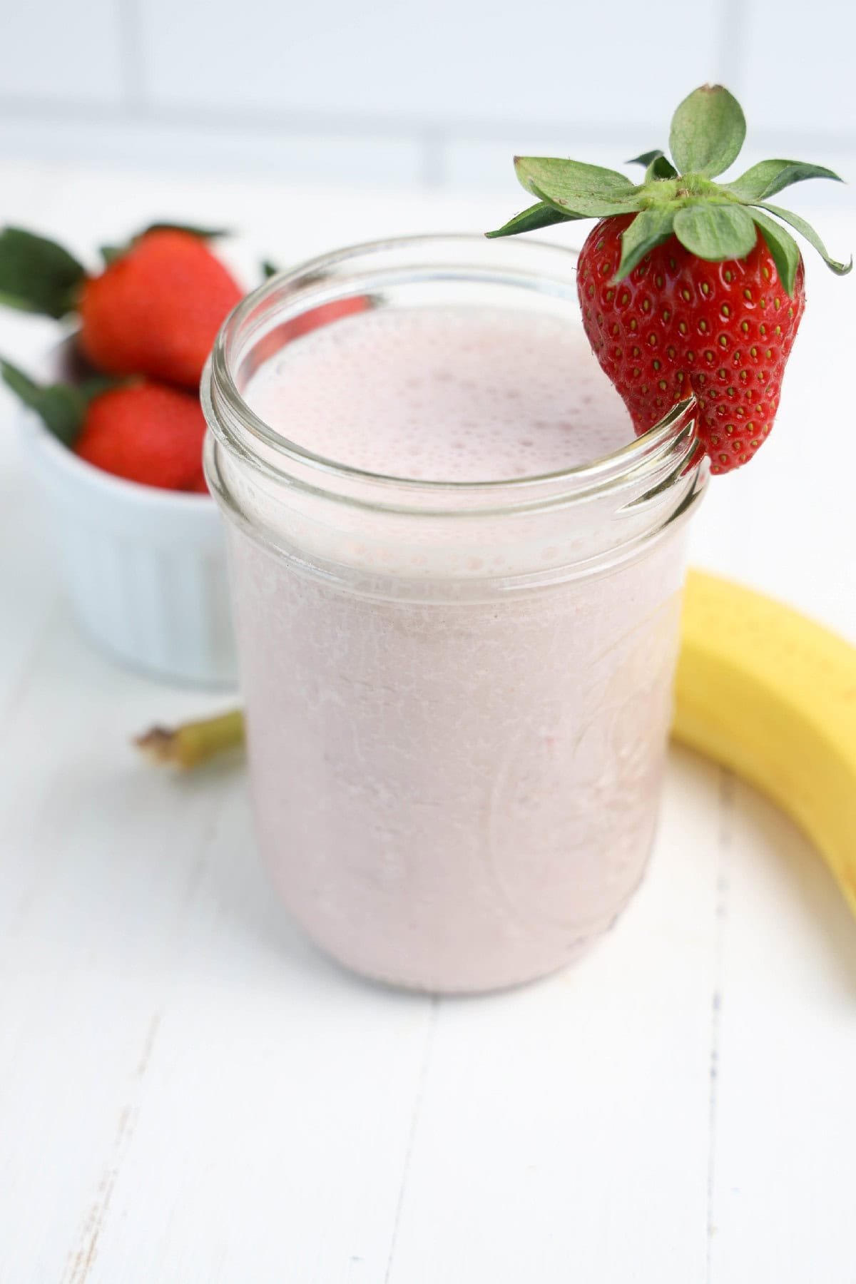 A creamy strawberry banana smoothie in a glass, with a strawberry on top for decoration.