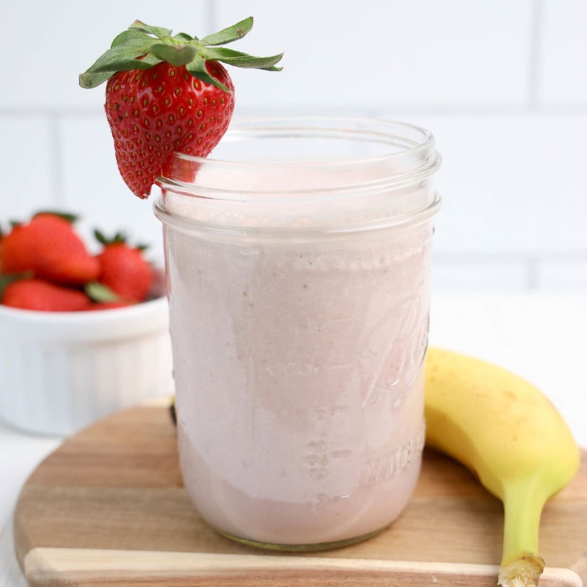 A colorful strawberry banana smoothie in a clear glass, showcasing a blend of strawberries and bananas on a cutting board.
