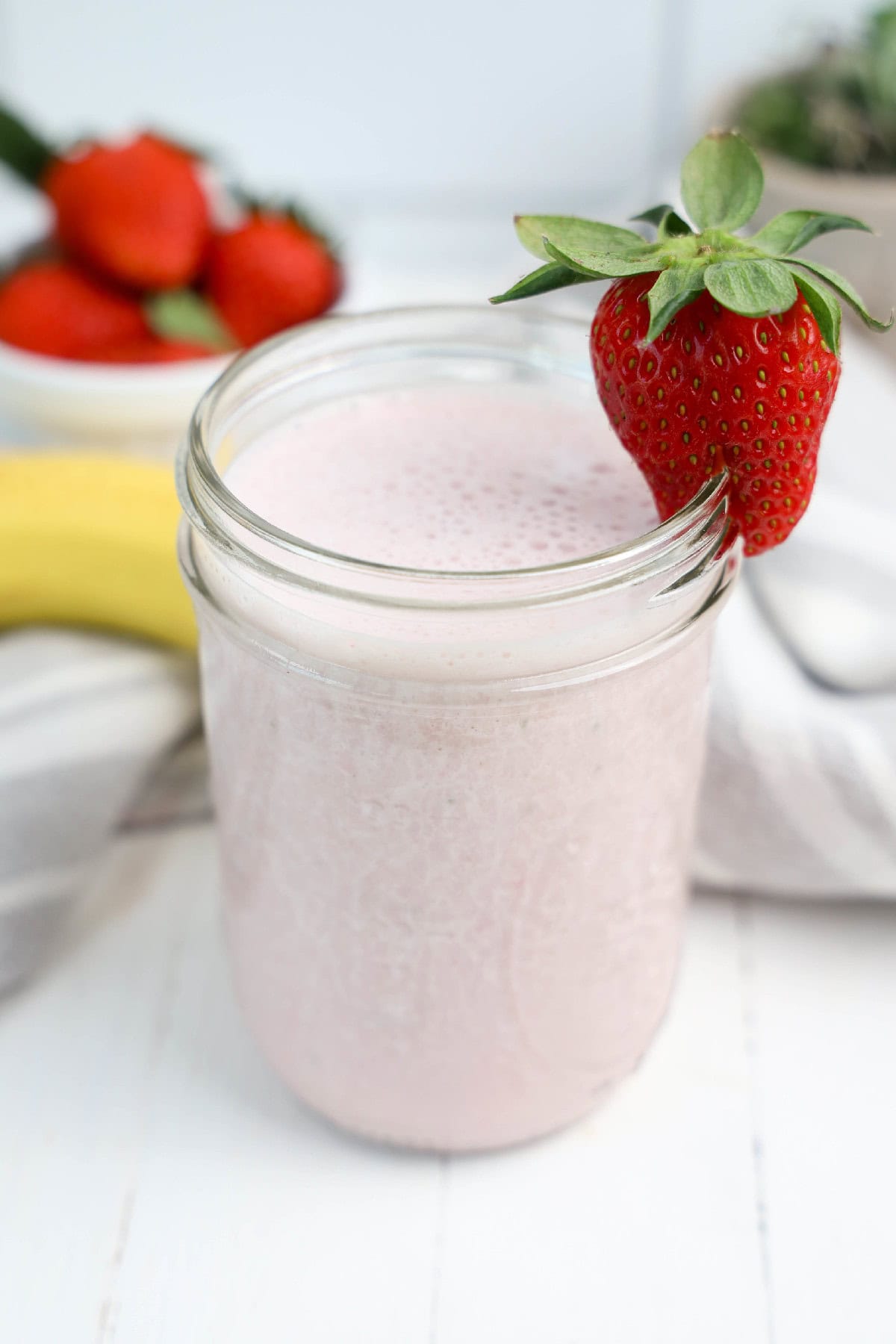 A vibrant pink strawberry banana smoothie in a glass, garnished with a strawberry on the rim.