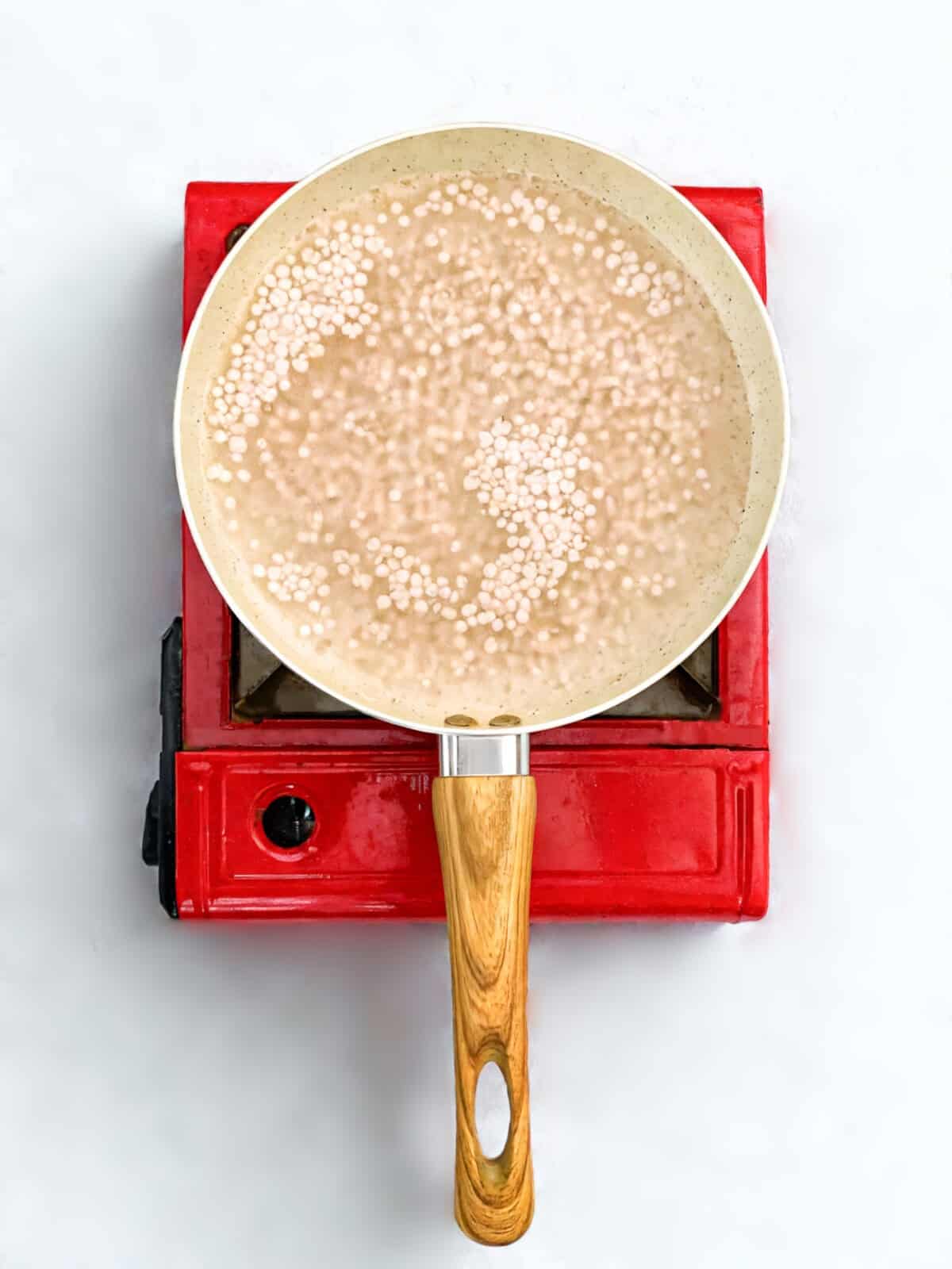 Boiling tapioca pearls in a beige nonstick pan over a red stovetop, preparing mango sago base.