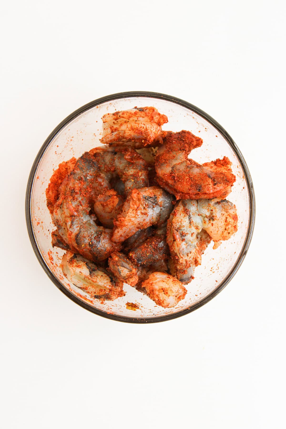 Raw shrimp tossed with blackened seasoning in a glass bowl.