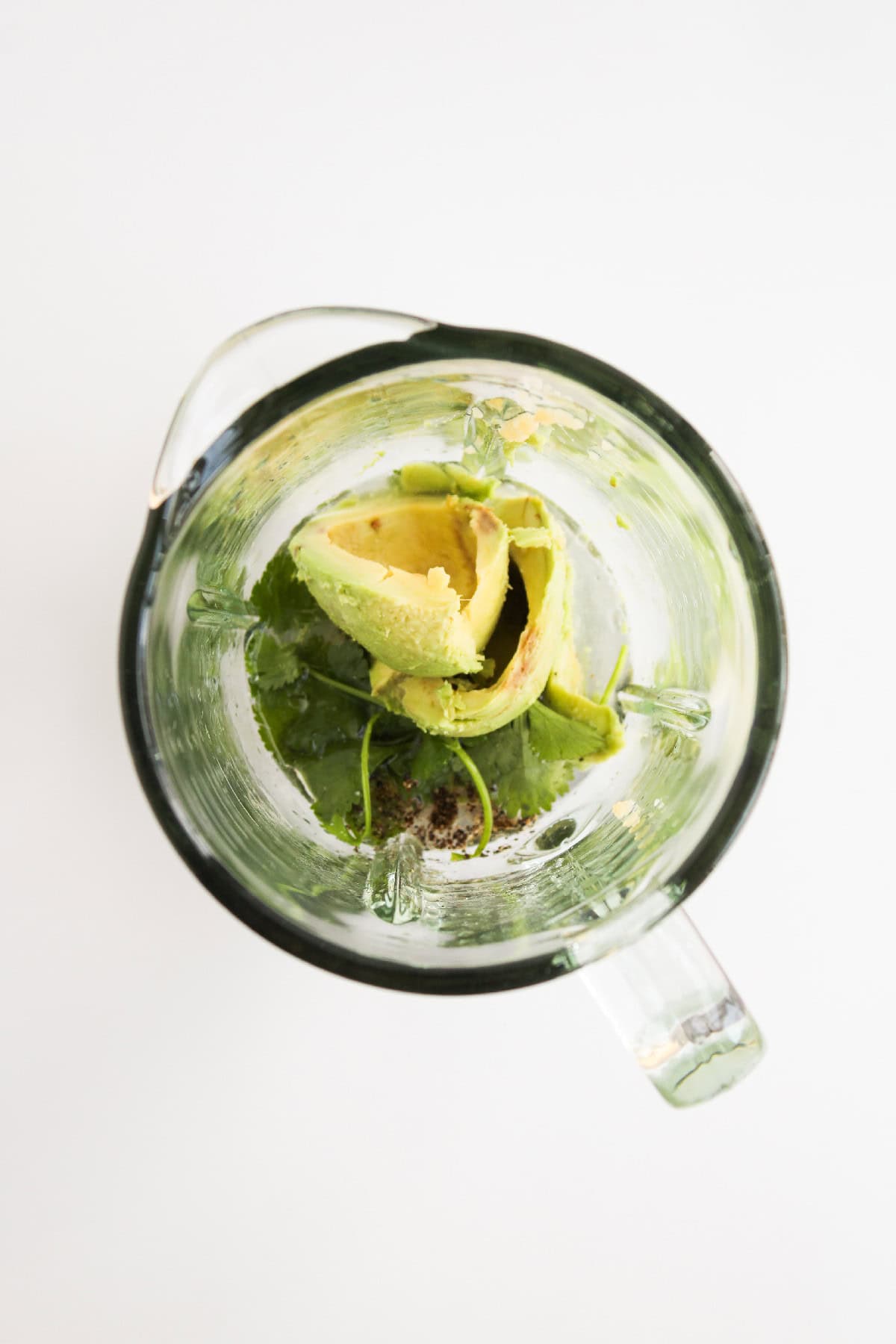 Fresh avocado, cilantro, and seasoning in a blender.