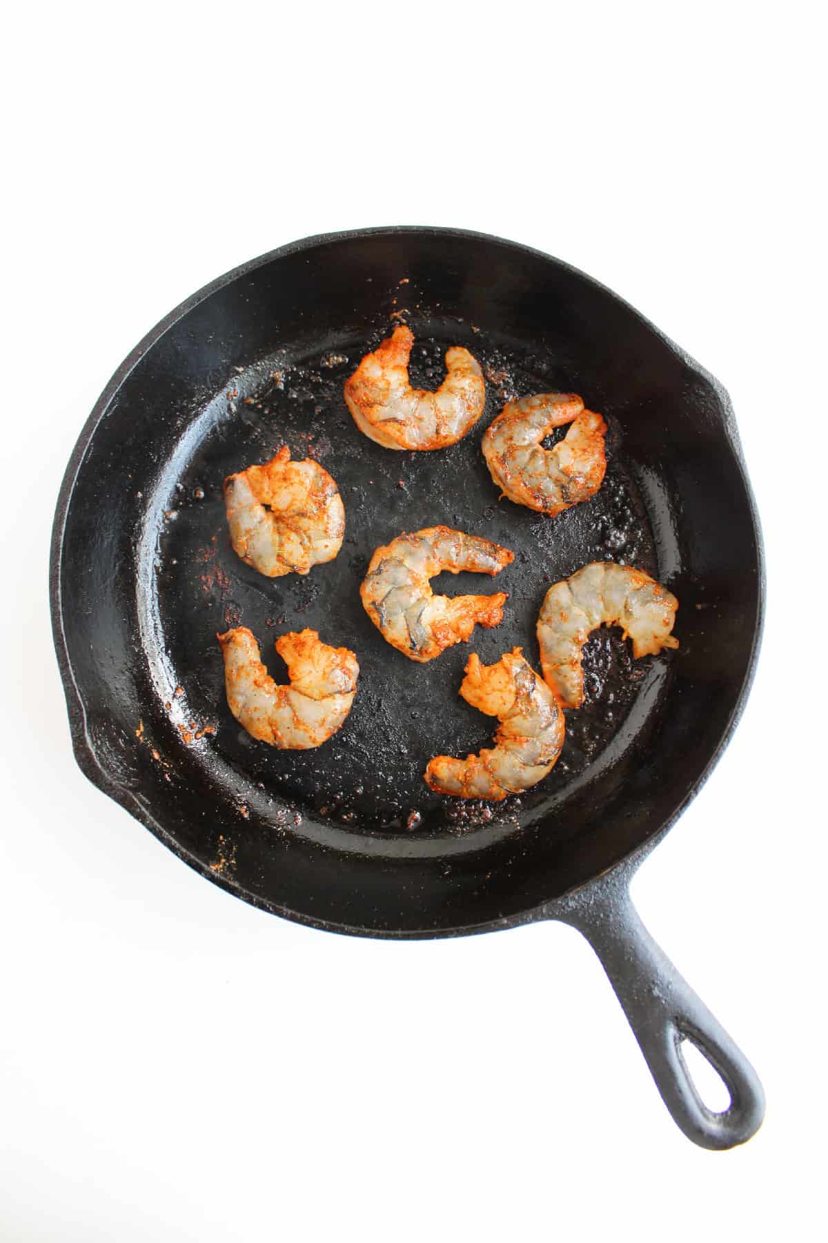 Seasoned shrimp beginning to cook in a hot cast iron skillet.