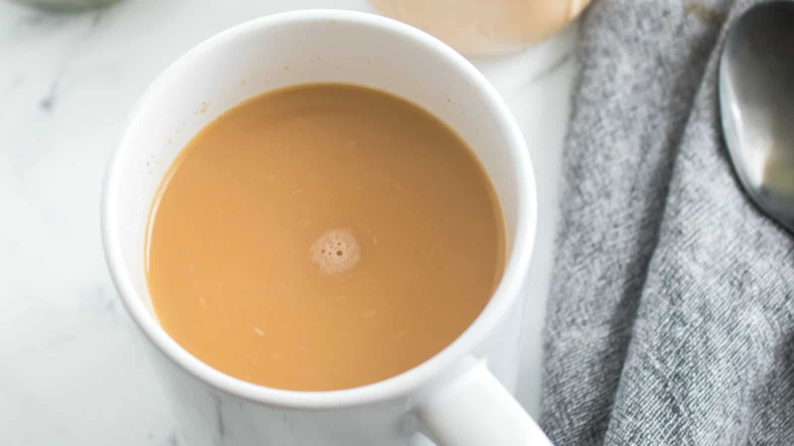 A steaming mug of coffee, mixed with pumpkin spice creamer, sits on a table.