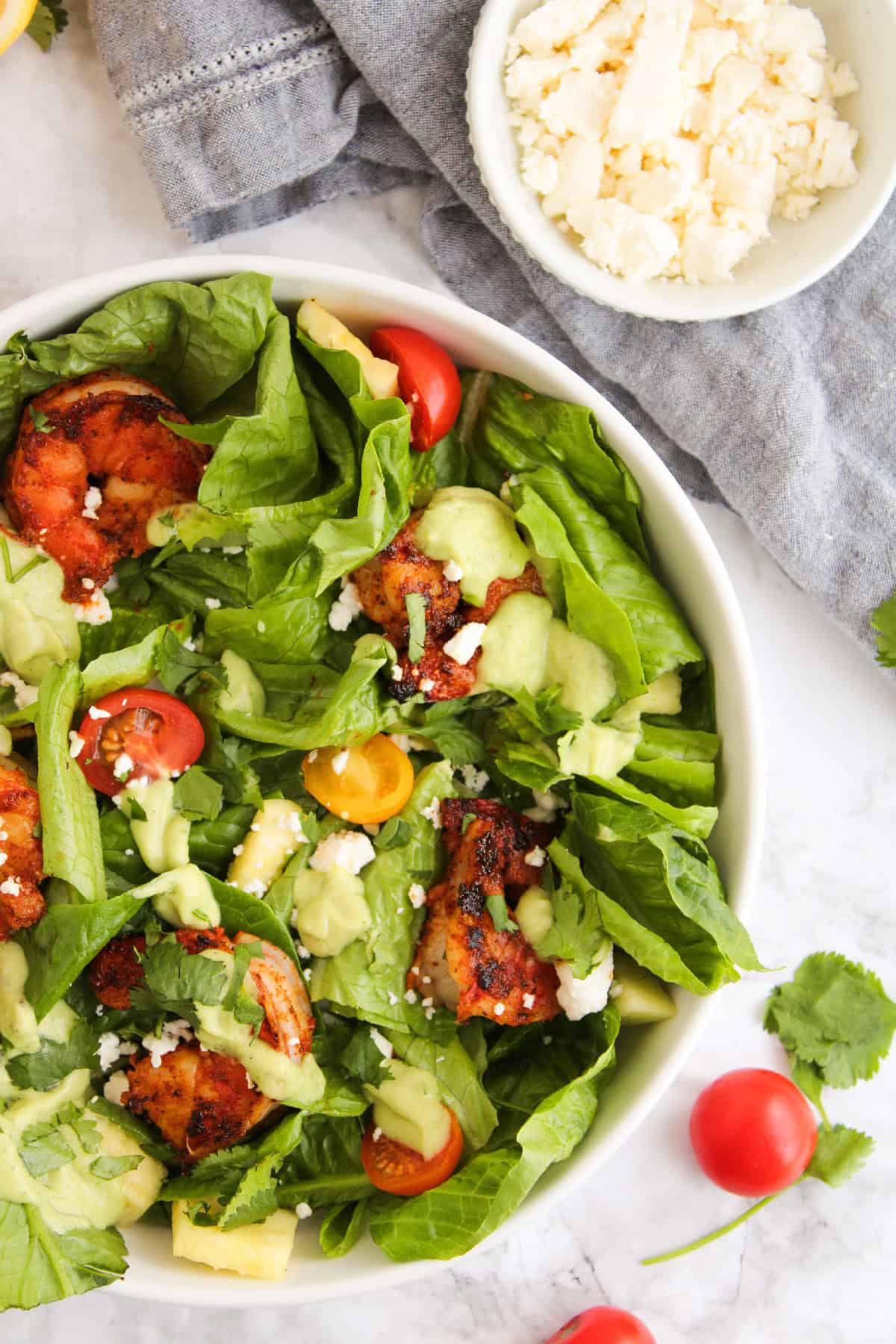 Close-up of a blackened shrimp salad with avocado dressing, cherry tomatoes, fresh romaine, feta cheese, and cilantro in a bowl.