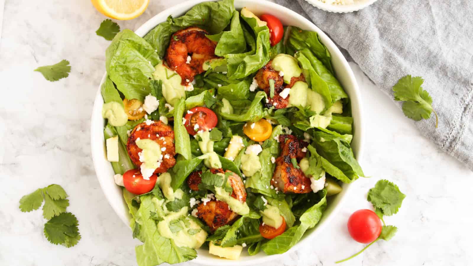 Blackened shrimp salad with avocado dressing, cherry tomatoes, feta cheese, and romaine lettuce in a light white bowl.