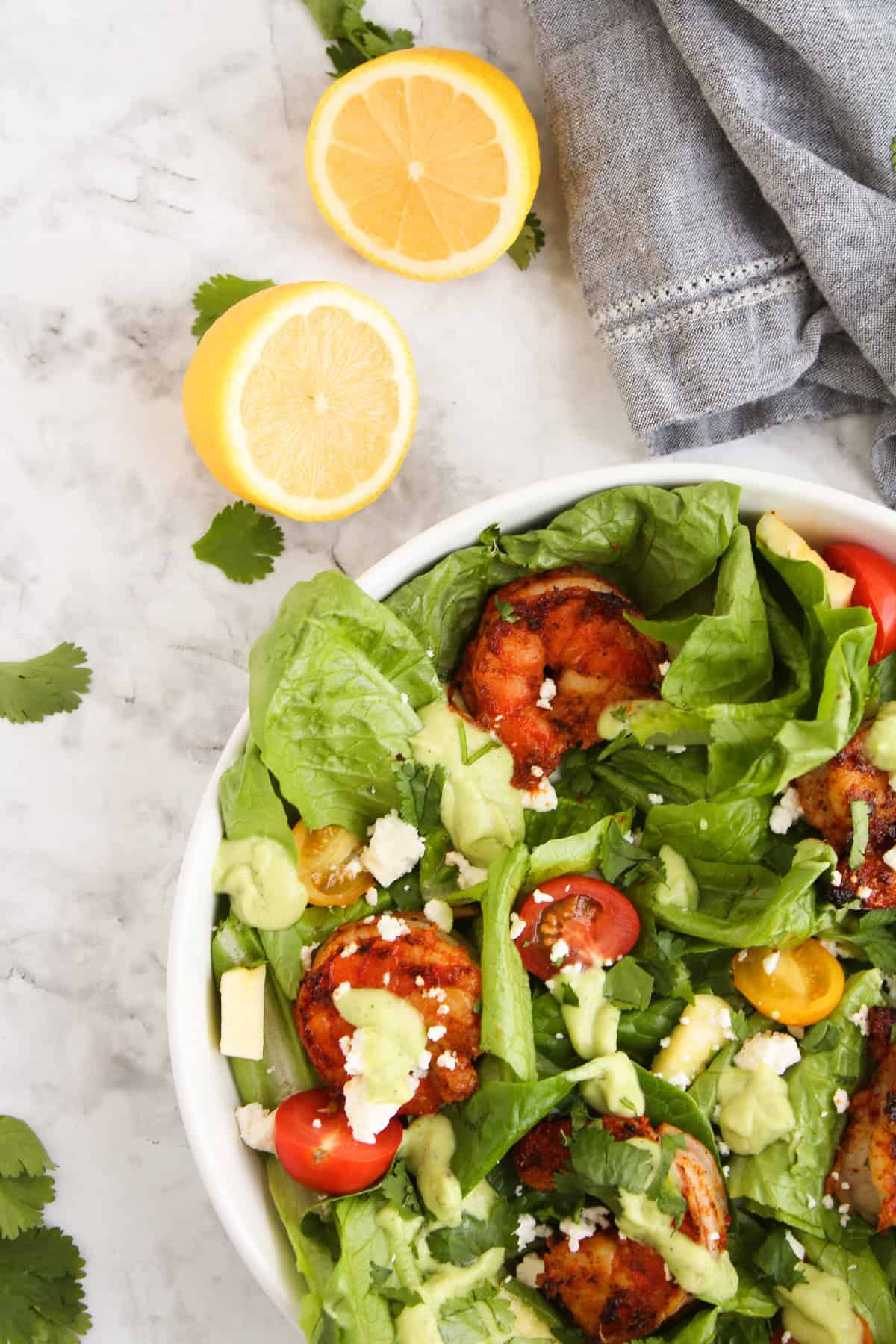 Close view of a blackened shrimp salad with avocado dressing, cherry tomatoes, fresh romaine, feta cheese, and cilantro in a white bowl.