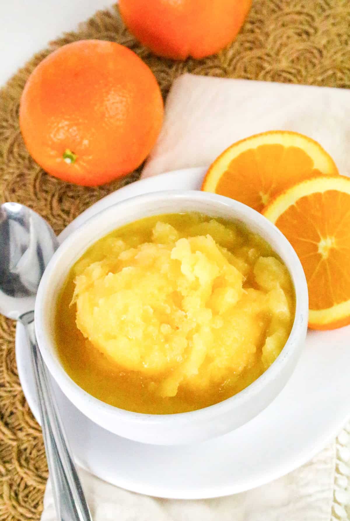 Homemade orange sorbet served in a white bowl with fresh oranges.
