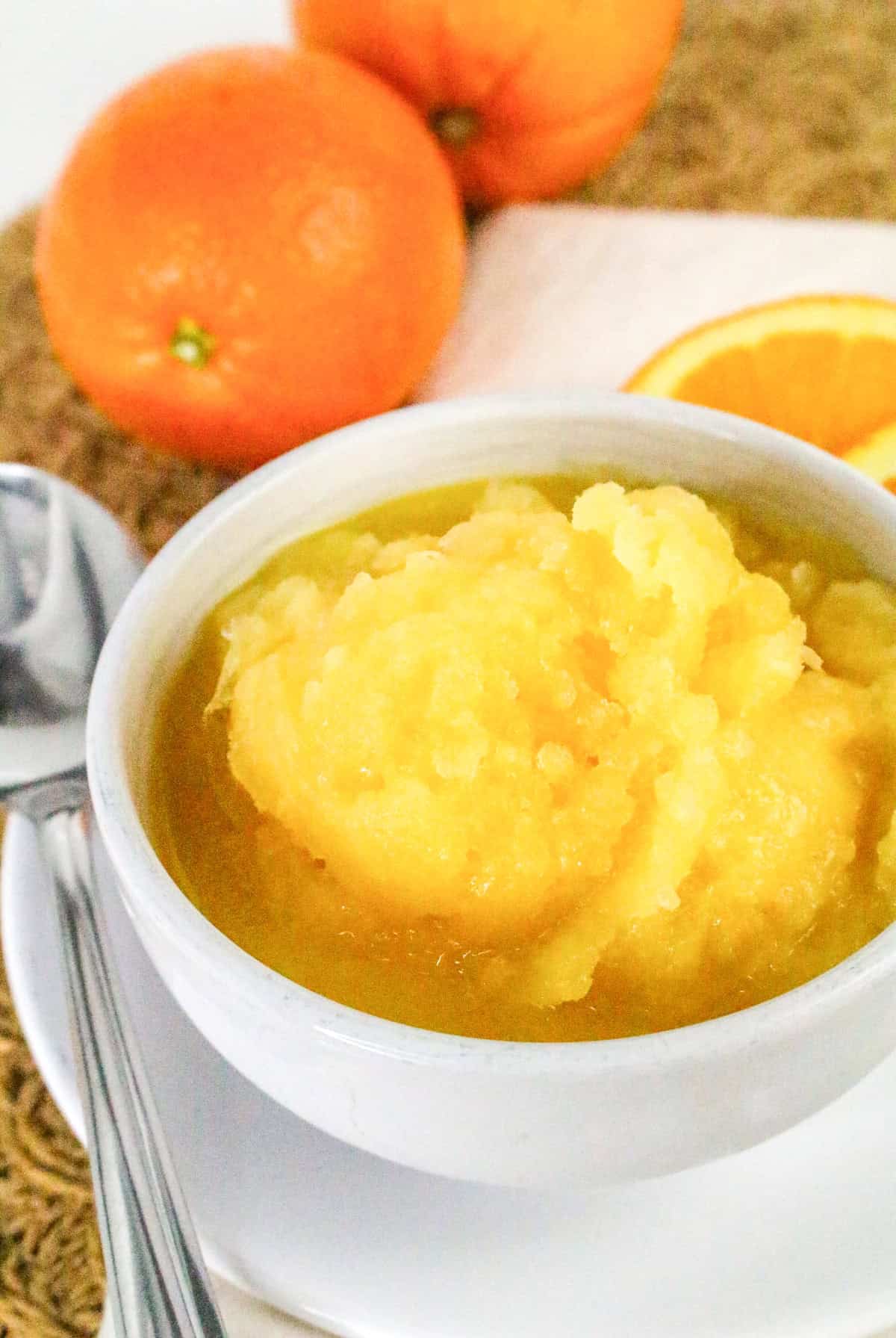 Orange sorbet served in a white bowl with fresh oranges.