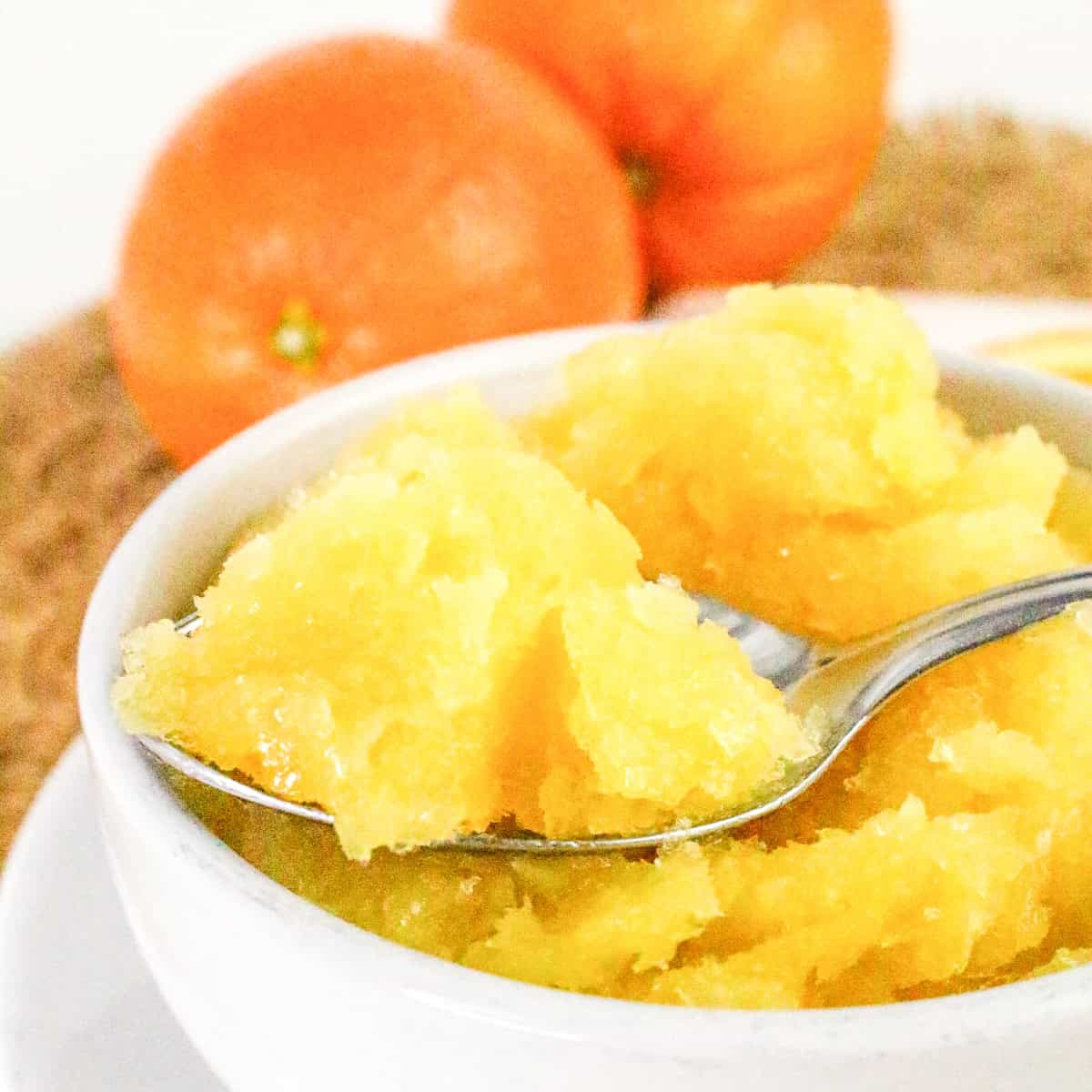 Spoonful of fresh orange sorbet lifted from a white bowl.