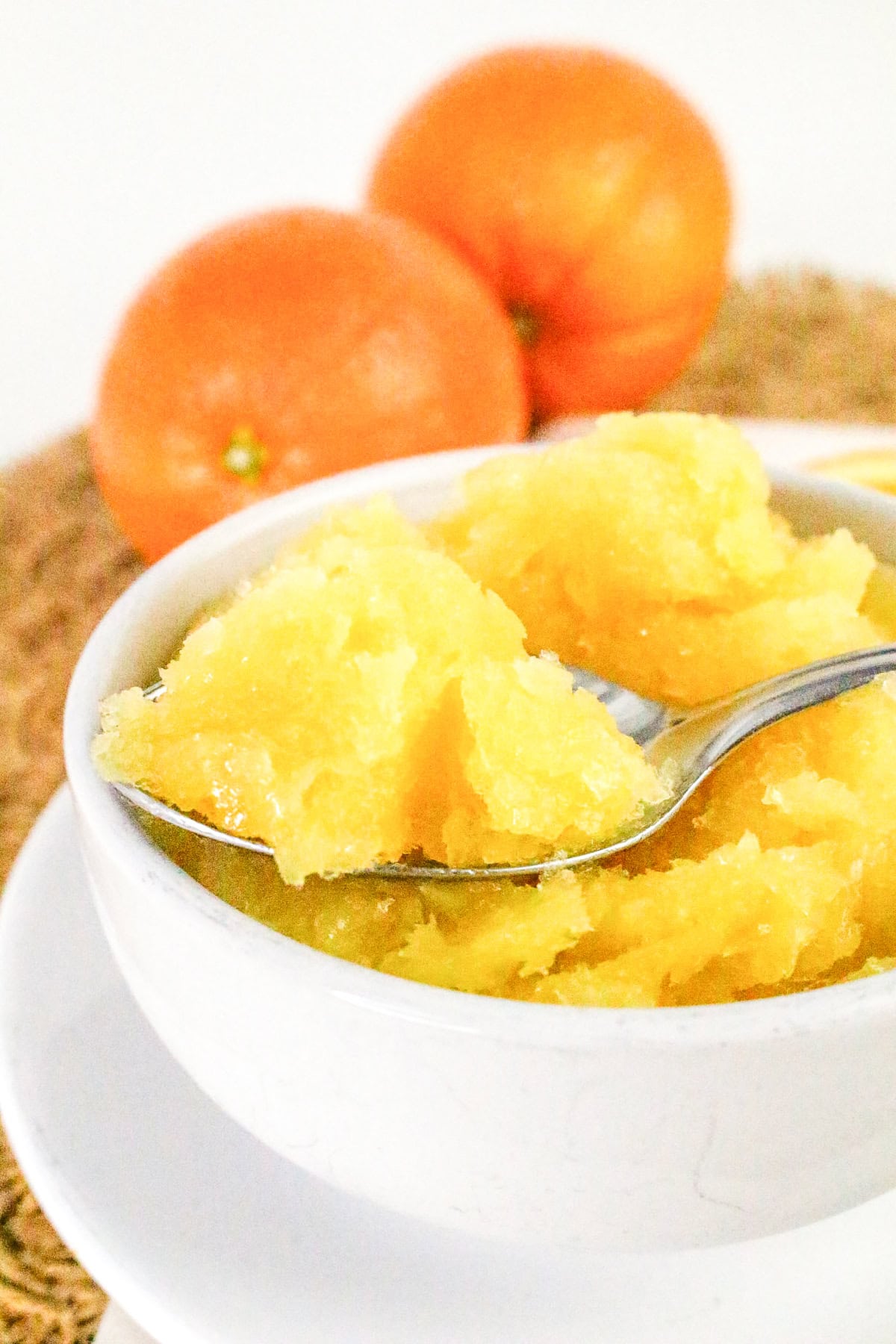 Spoonful of fresh orange sorbet lifted from a white bowl, with whole oranges in the background.