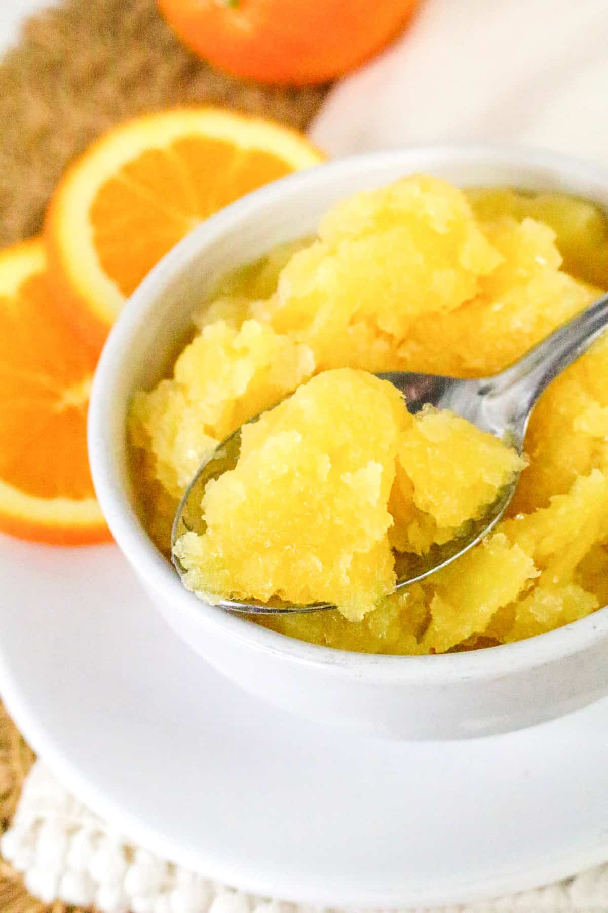 Spoon scooping a soft bite of orange sorbet from a white bowl.