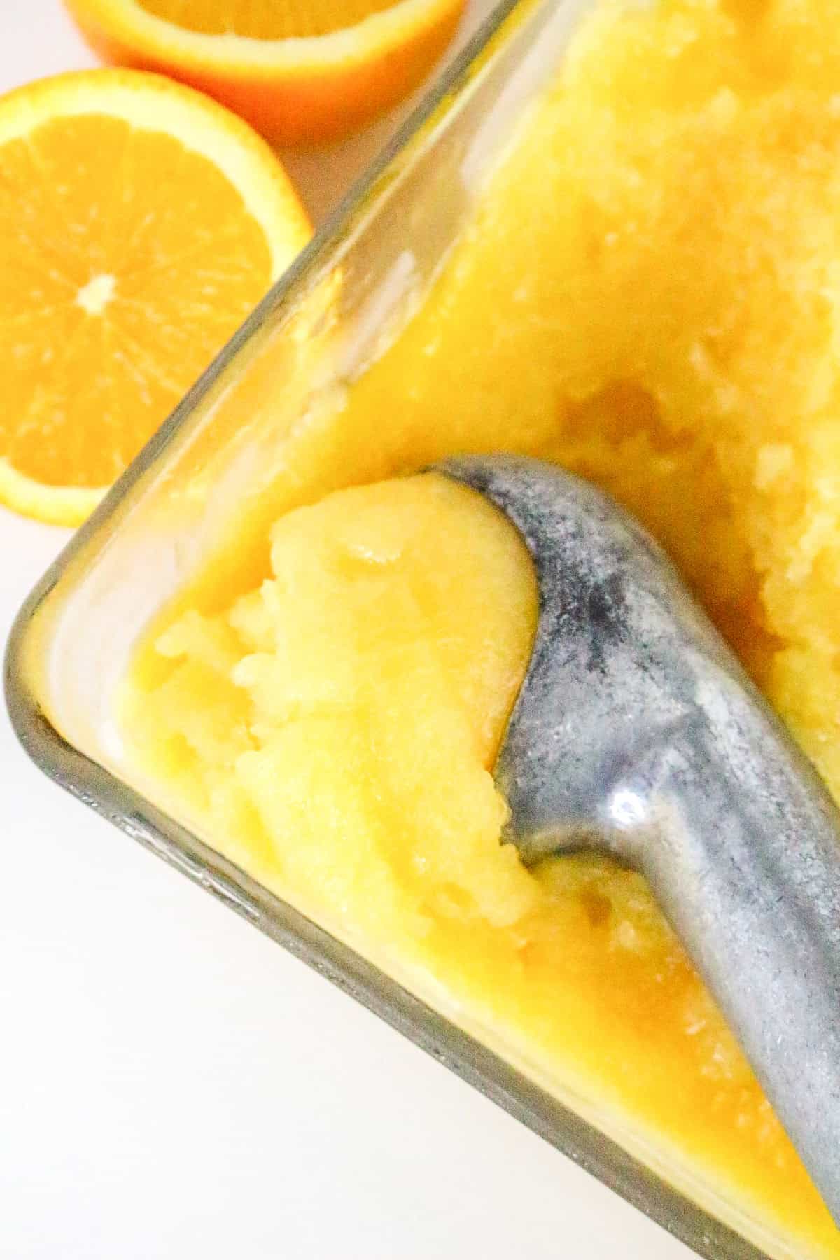 Scooping homemade orange sorbet from glass dish.