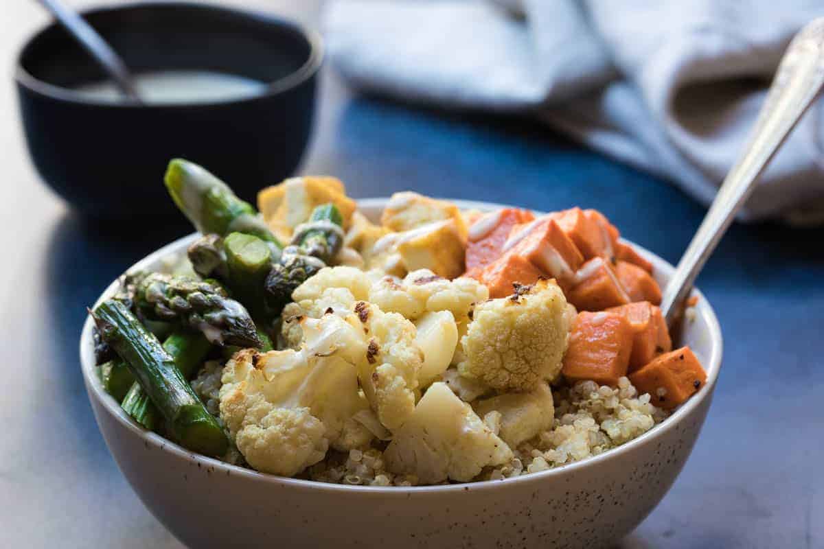 Colorful vegan Buddha bowl with grains, veggies, and lemon tahini dressing.
