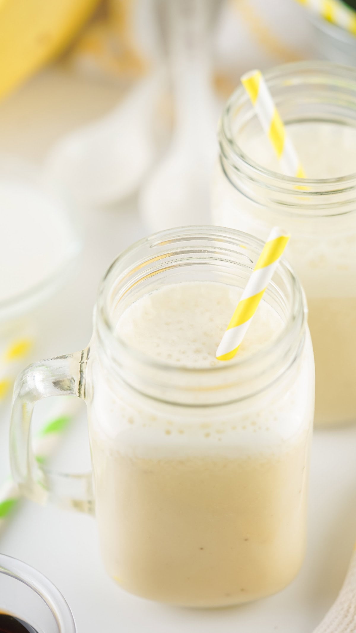 Close-up view of banana milk foam in a mason jar with a yellow-striped straw, showcasing creamy texture.