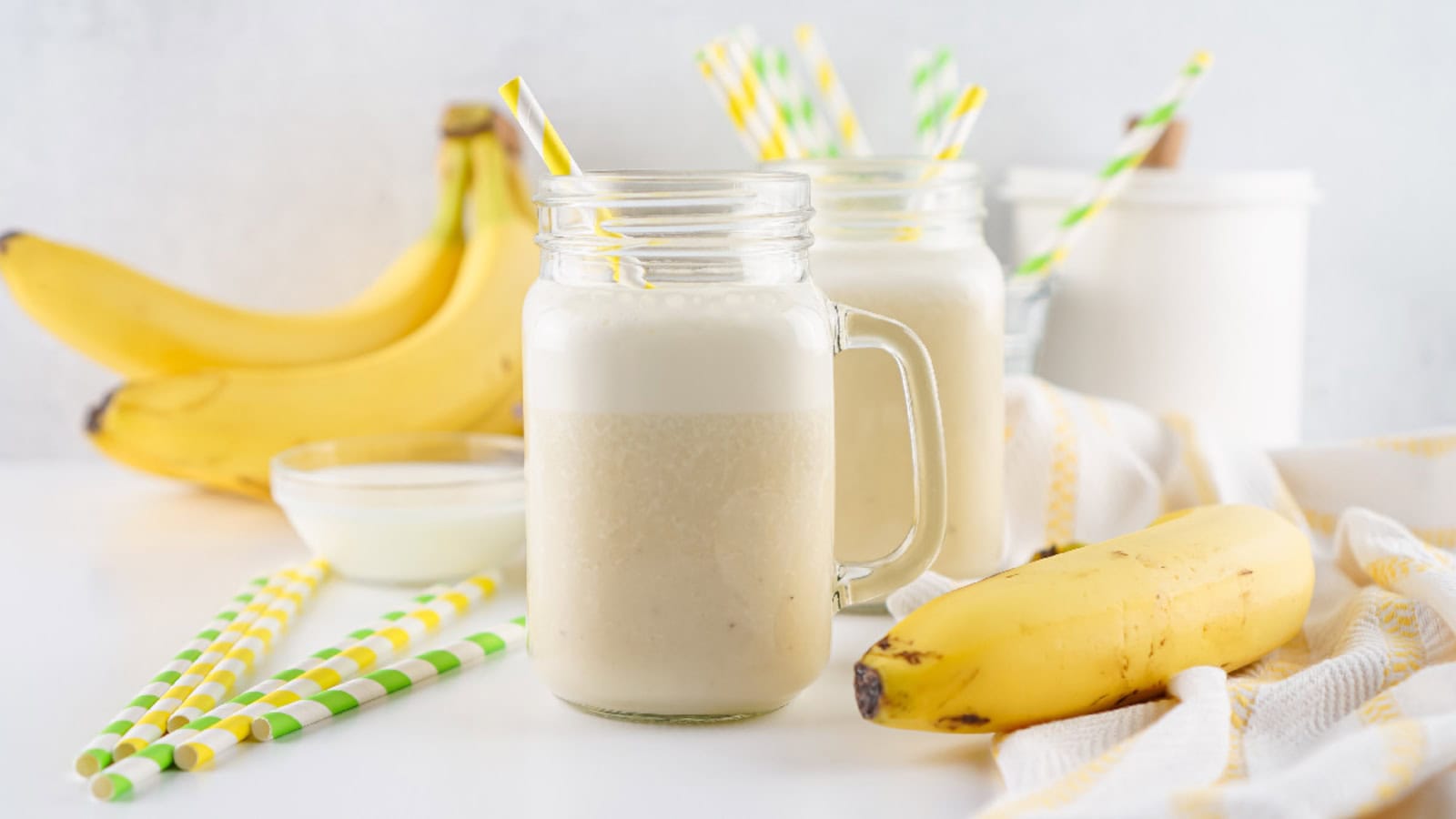 Creamy homemade banana milk in mason jar glasses with light yellow striped straws.