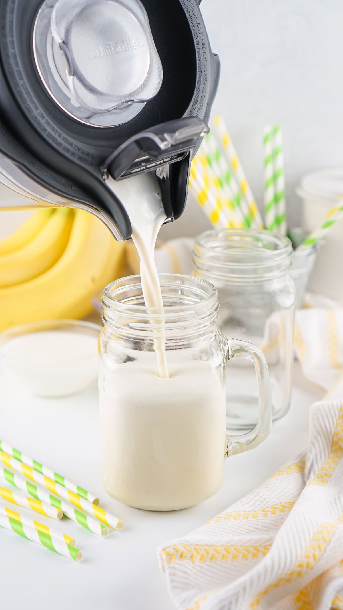 Creamy banana milk being poured from Nutribullet blender into a mason jar glass.