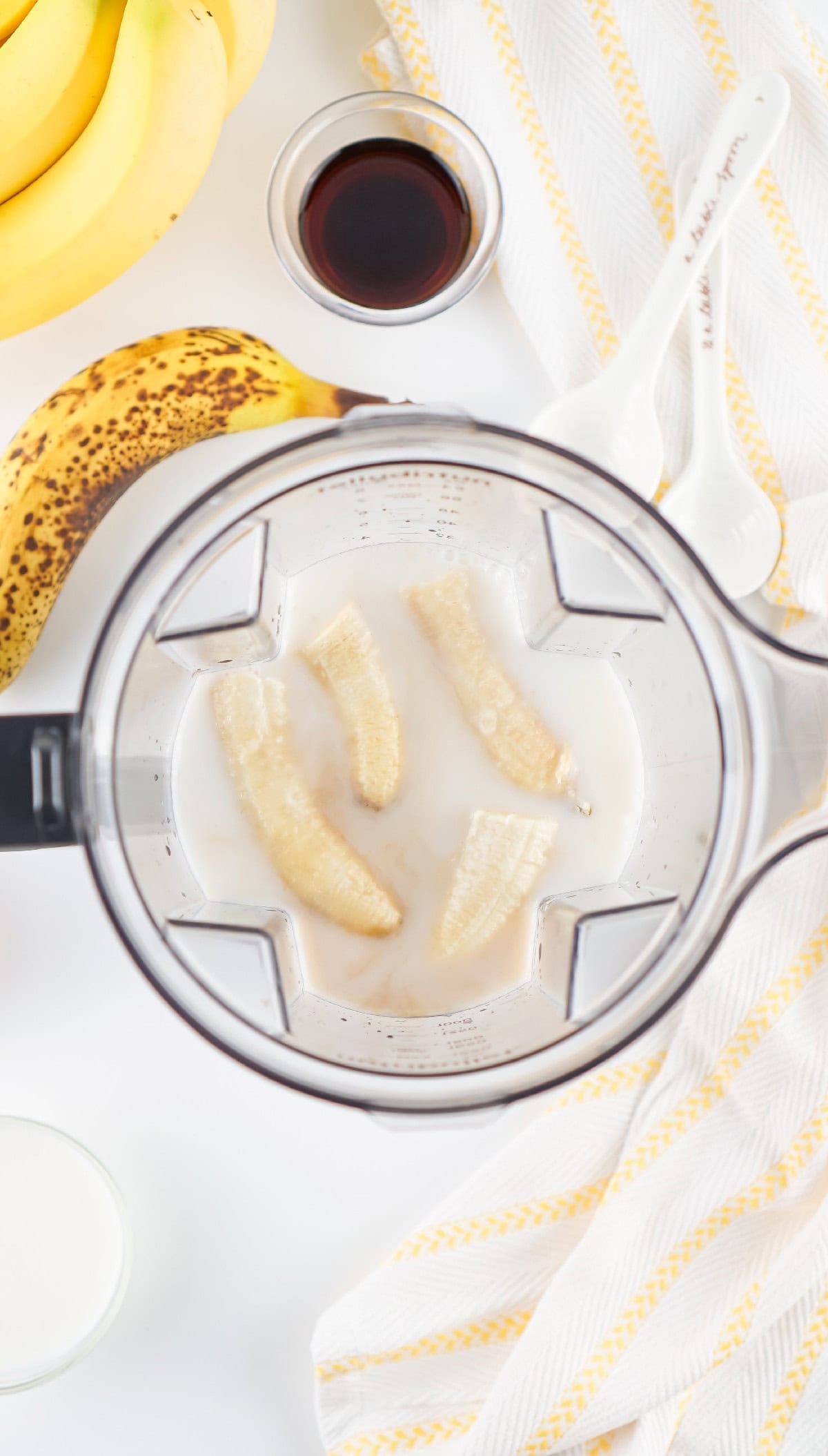 Blender filled with bananas, milk, water, maple syrup, and vanilla extract before blending.