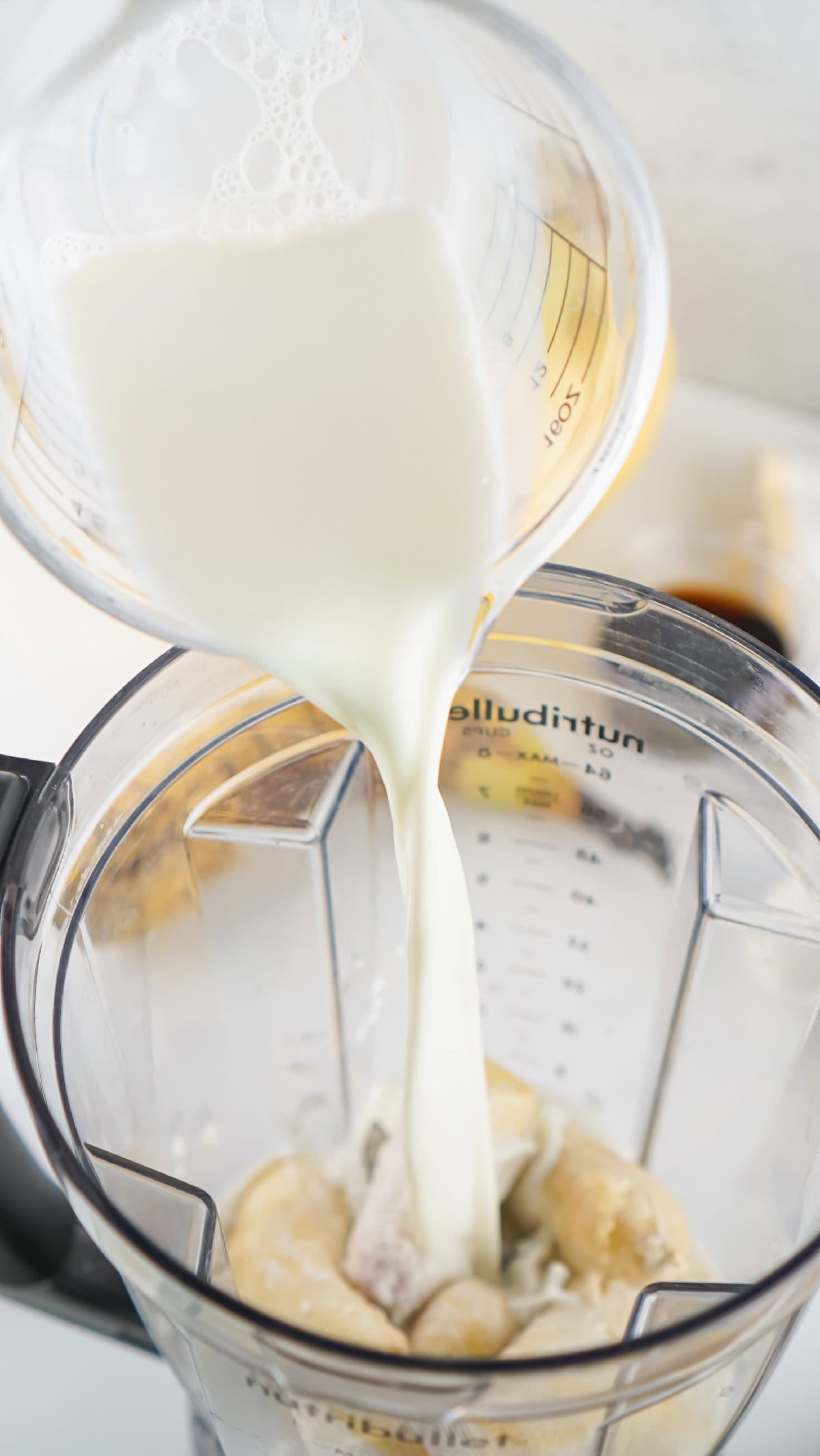 Fresh milk being poured into a blender with bananas for homemade banana milk.