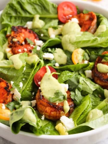 Blackened shrimp salad with avocado dressing, cherry tomatoes, feta cheese, and romaine lettuce in a white bowl.