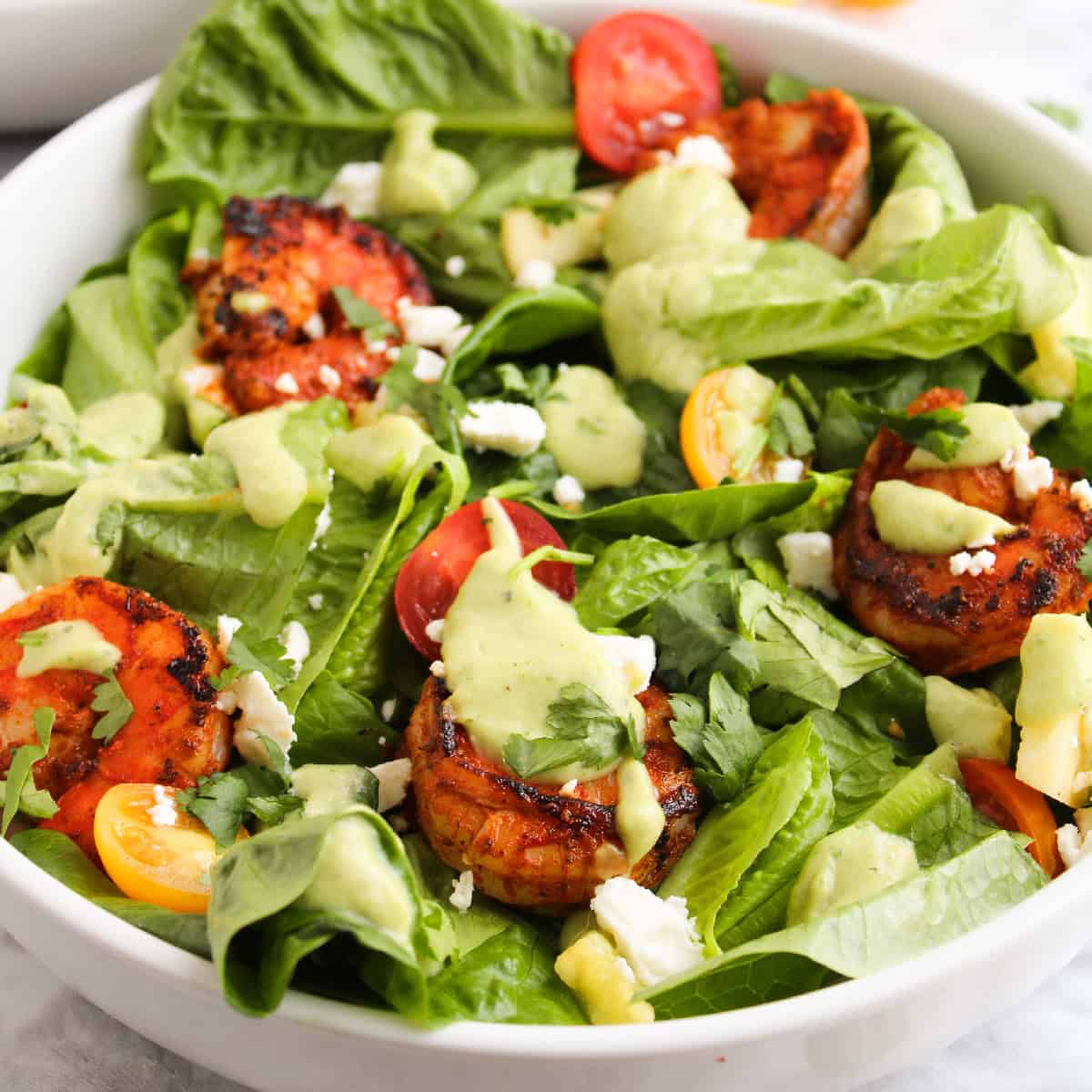 Blackened shrimp salad with avocado dressing, cherry tomatoes, feta cheese, and romaine lettuce in a white bowl.