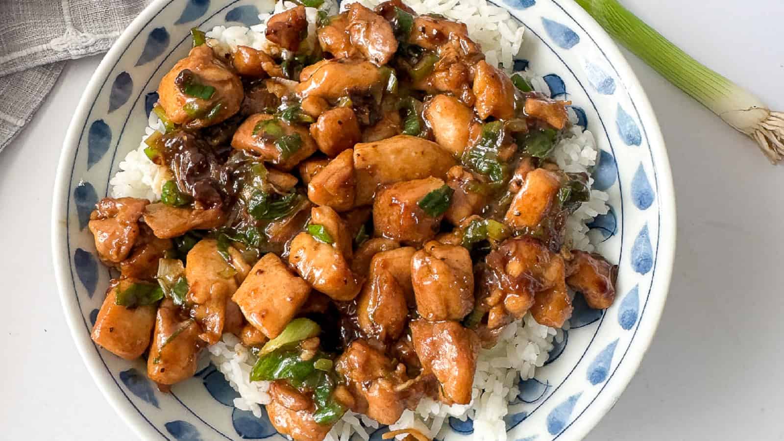 A bowl of cooked Chinese scallion chicken served in a white and blue bowl.
