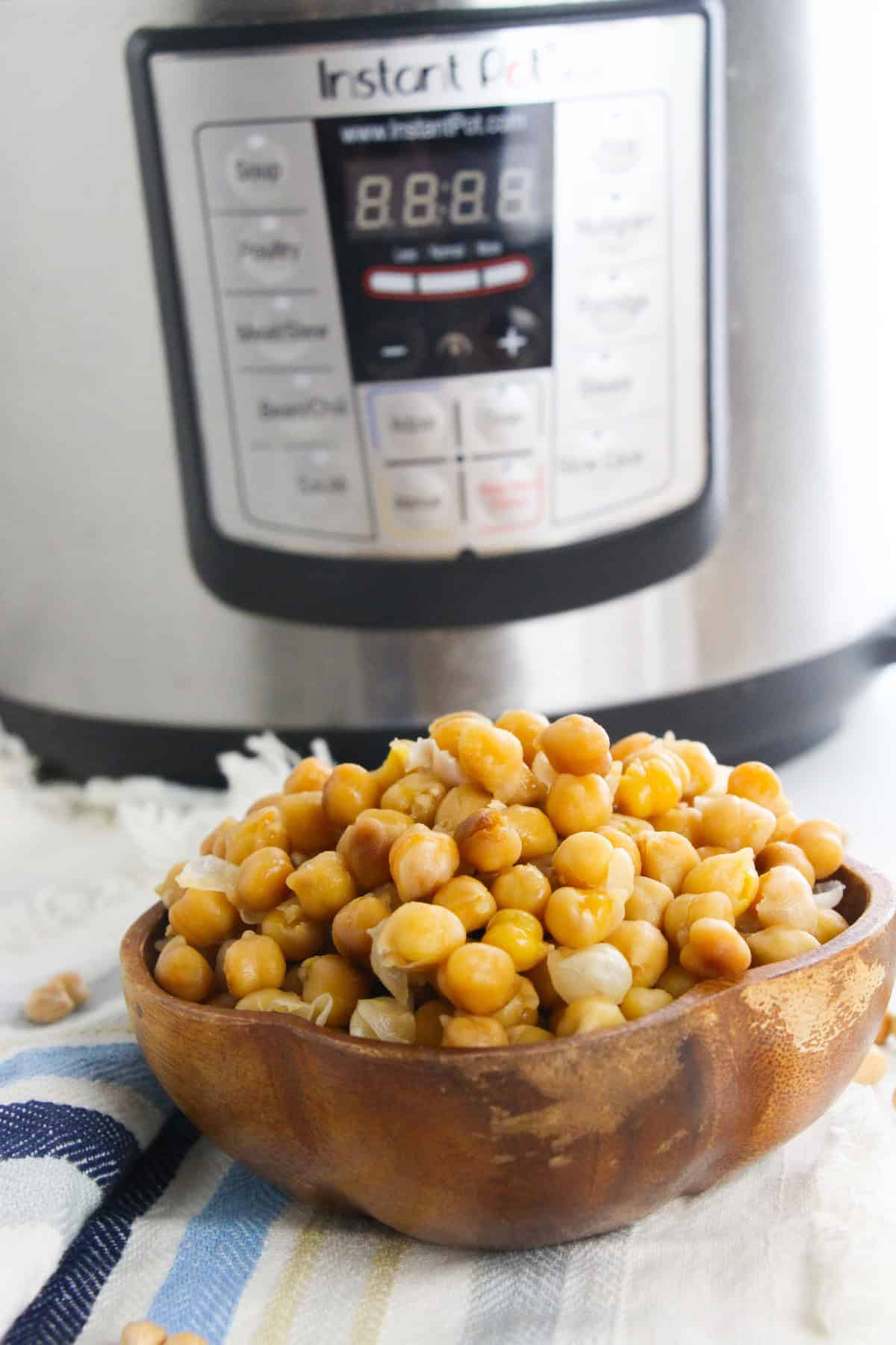 Cooked chickpeas in a wooden bowl placed in front of an Instant Pot.