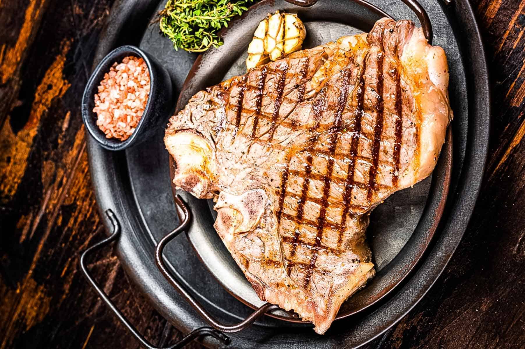 A grilled t-bone steak on a black platter.