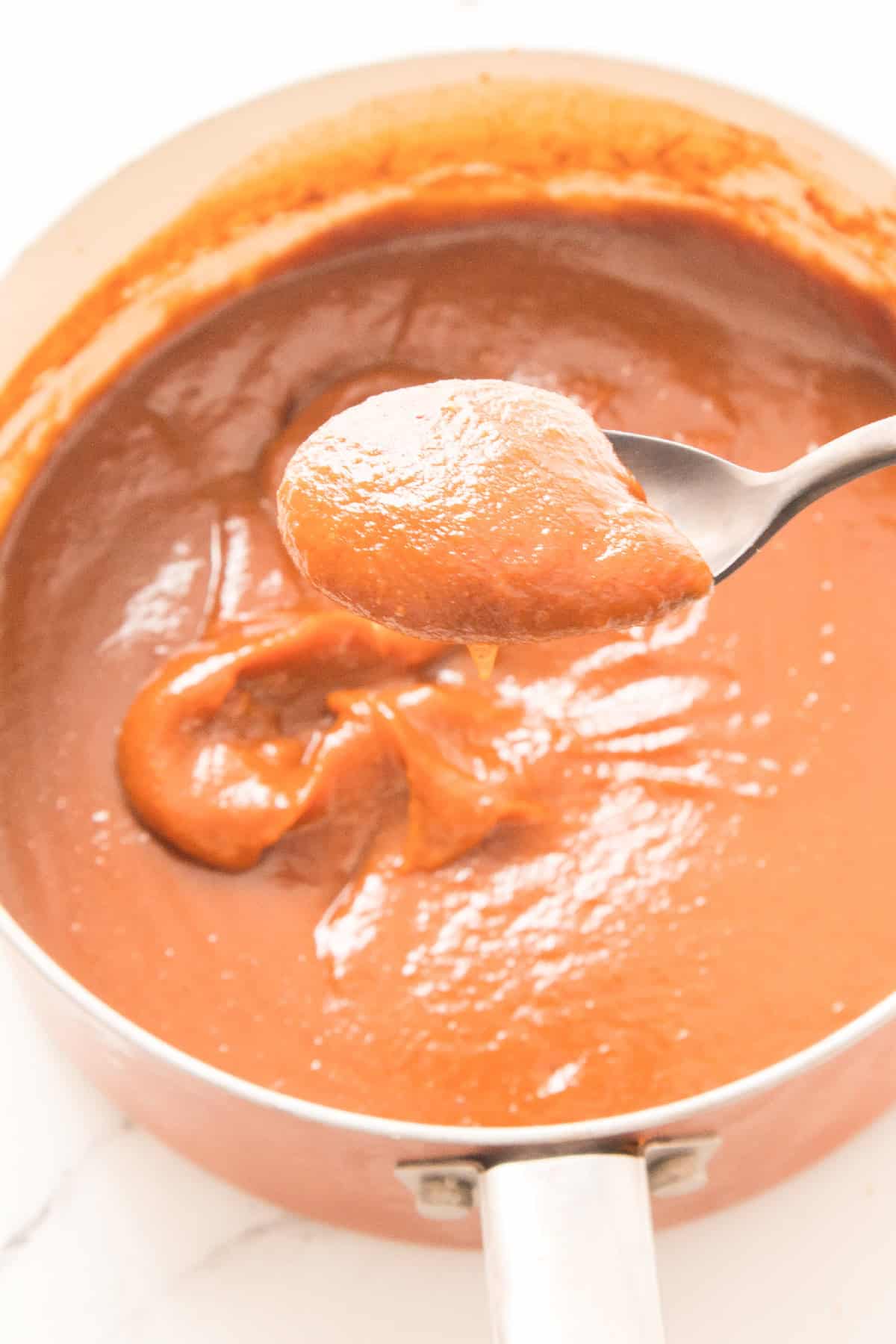 Freshly cooked pumpkin butter on a spoon above a saucepan.