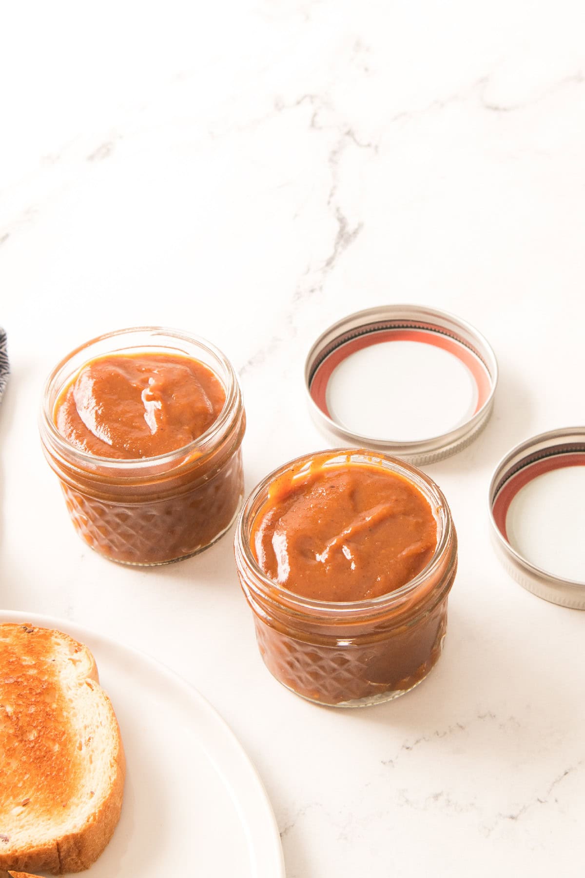 Small glass jars filled with pumpkin butter next to toasted bread.