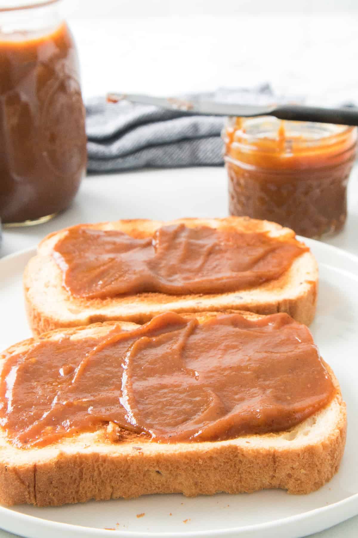 Side view of toast spread with pumpkin butter and jars in background.