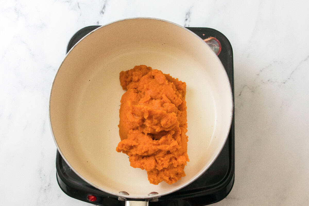 Pumpkin puree added to a saucepan on the stovetop.