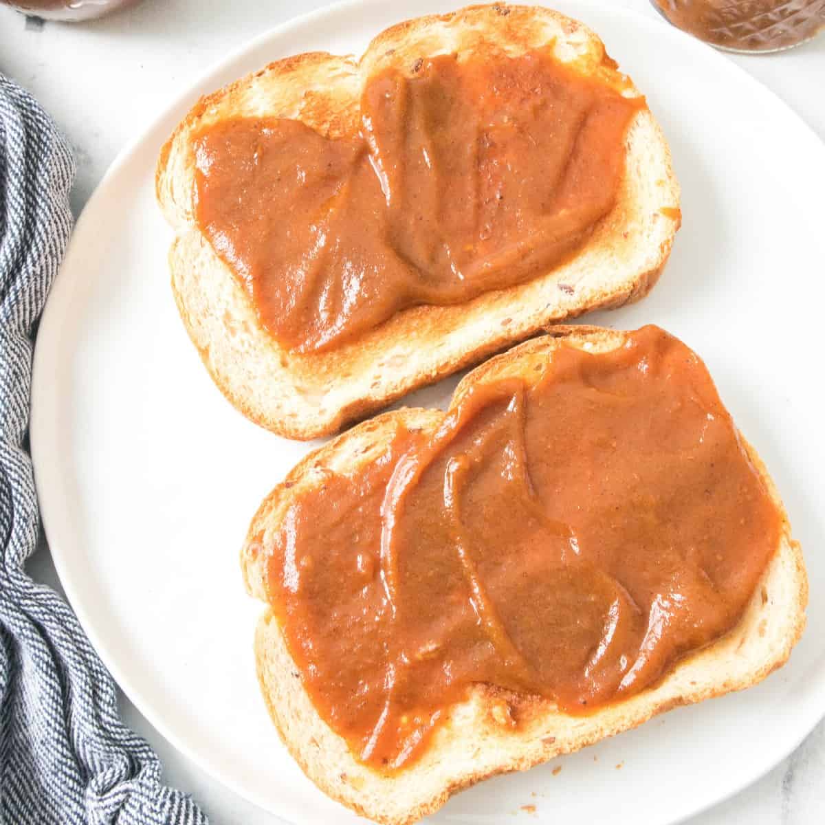 Pumpkin butter spread on toast with jars and a knife in the background.