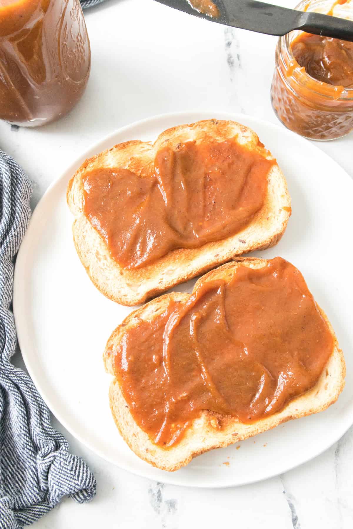 Pumpkin butter on toast with jars and knife styled on marble background.