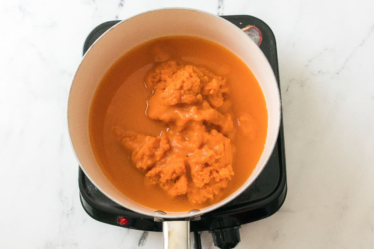 Pumpkin puree simmering with liquid in a saucepan.