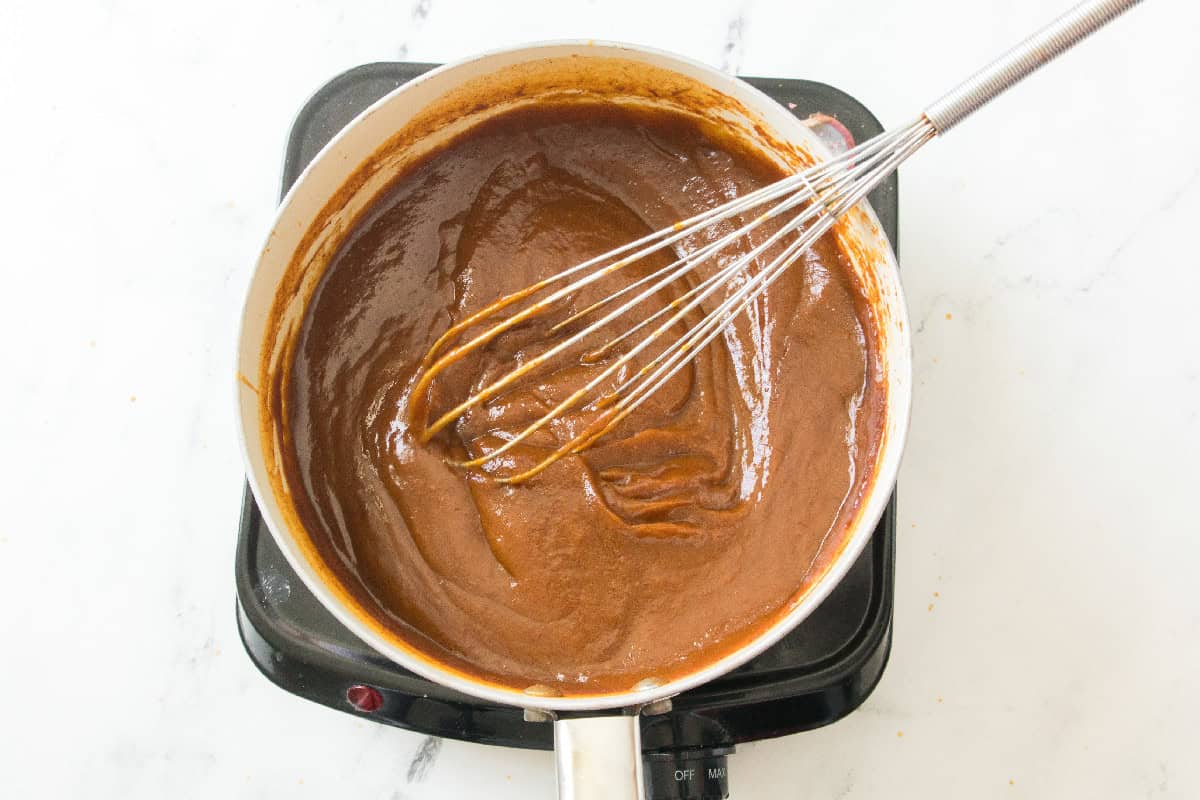 Pumpkin butter simmering and thickening with a whisk in the pot.