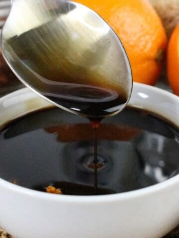 Spoon drizzling rich teriyaki orange sauce into a white bowl.