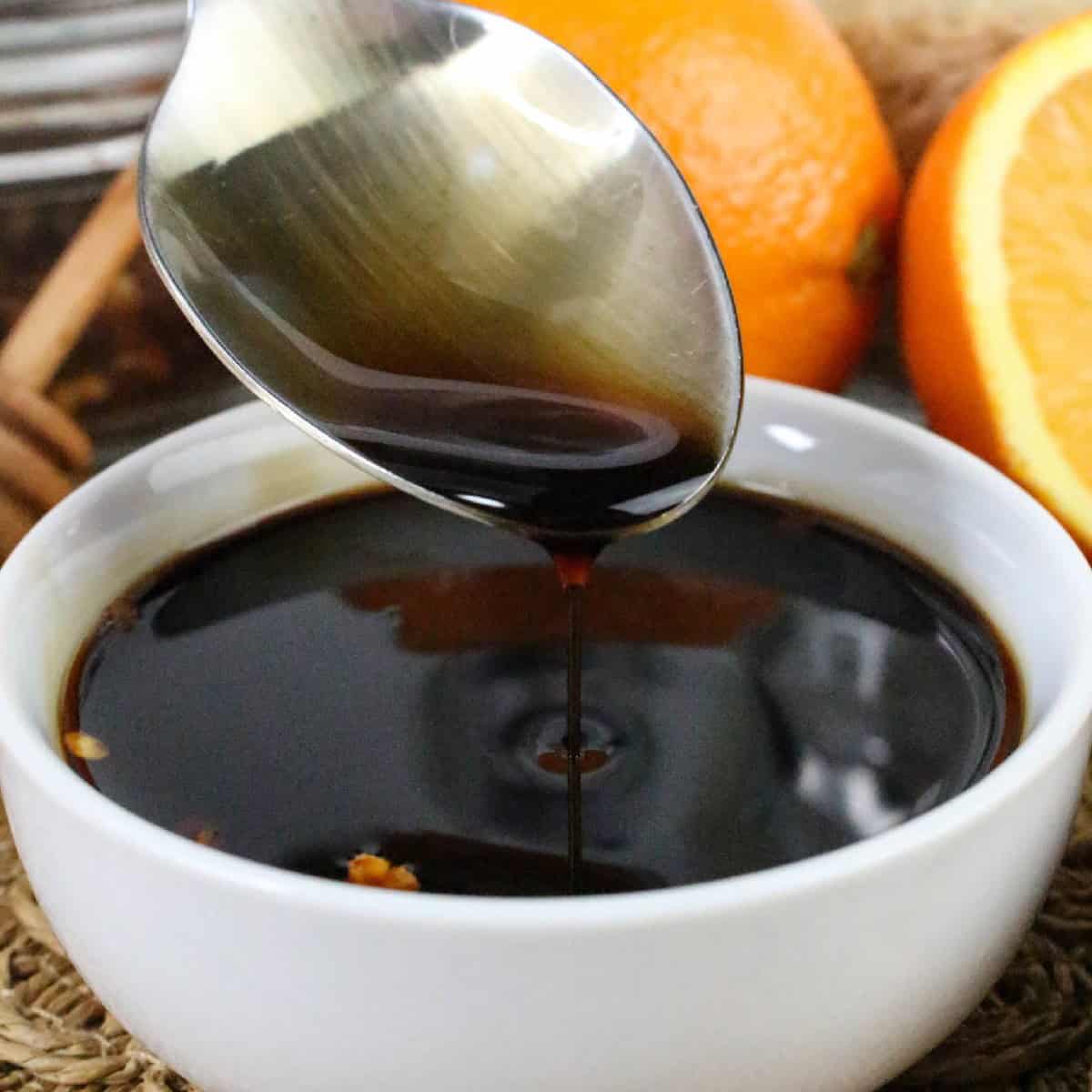 Spoon drizzling rich teriyaki orange sauce into a white bowl.
