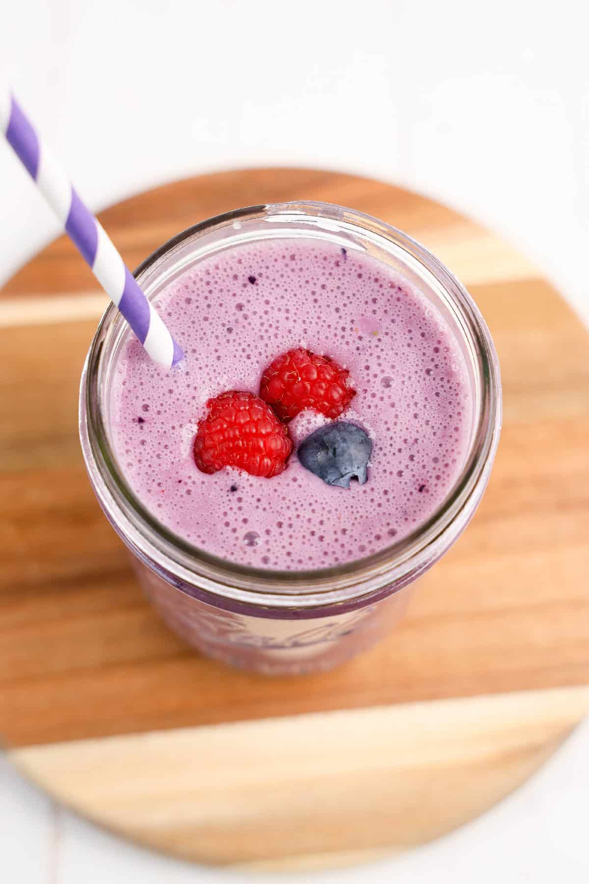 Overhead view of a vibrant purple vegan triple berry smoothie in a mason jar, topped with fresh raspberries and a blueberry.