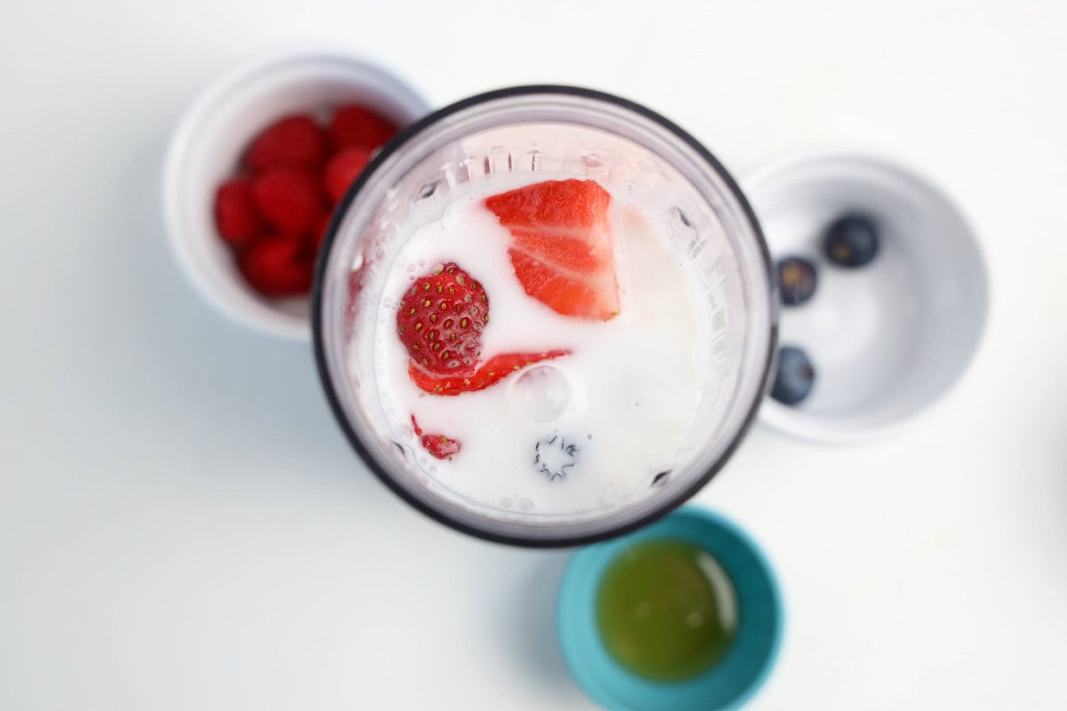 Strawberries and blueberries added to coconut milk in a blender cup.