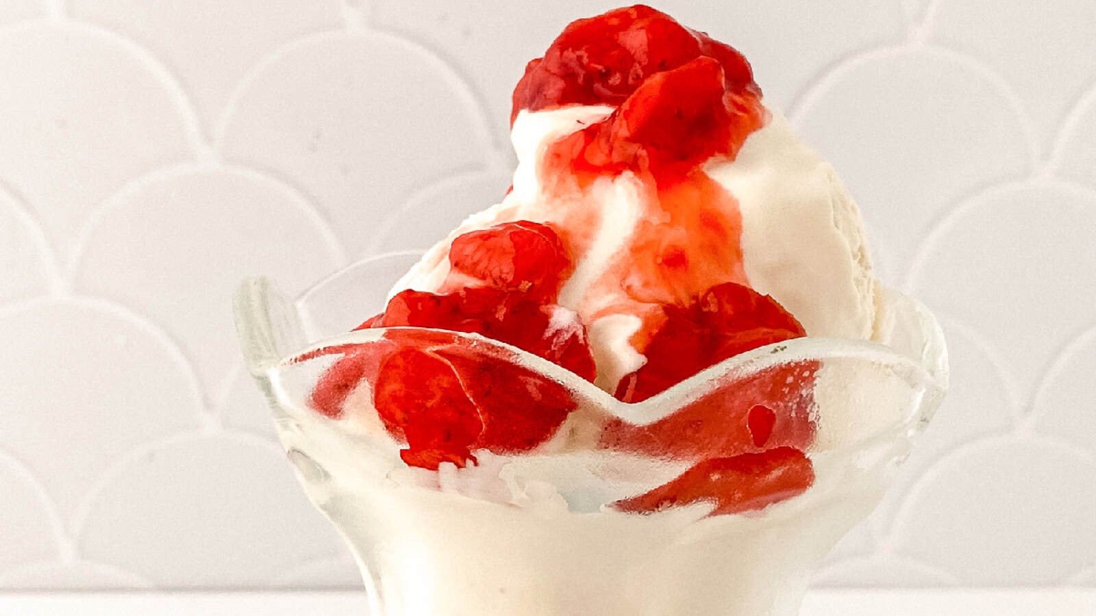 Close-up of vanilla bean ice cream sundae drizzled with strawberry topping.