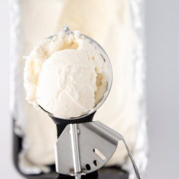 Close-up of creamy vanilla bean ice cream in a metal scoop above a pan.