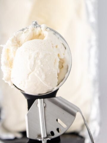Close-up of creamy vanilla bean ice cream in a metal scoop above a pan.