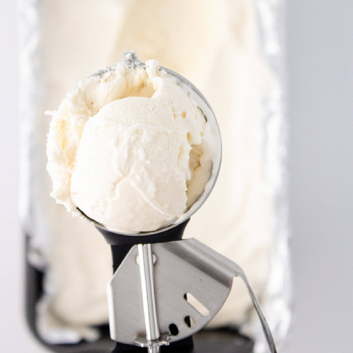 Close-up of creamy vanilla bean ice cream in a metal scoop above a pan.