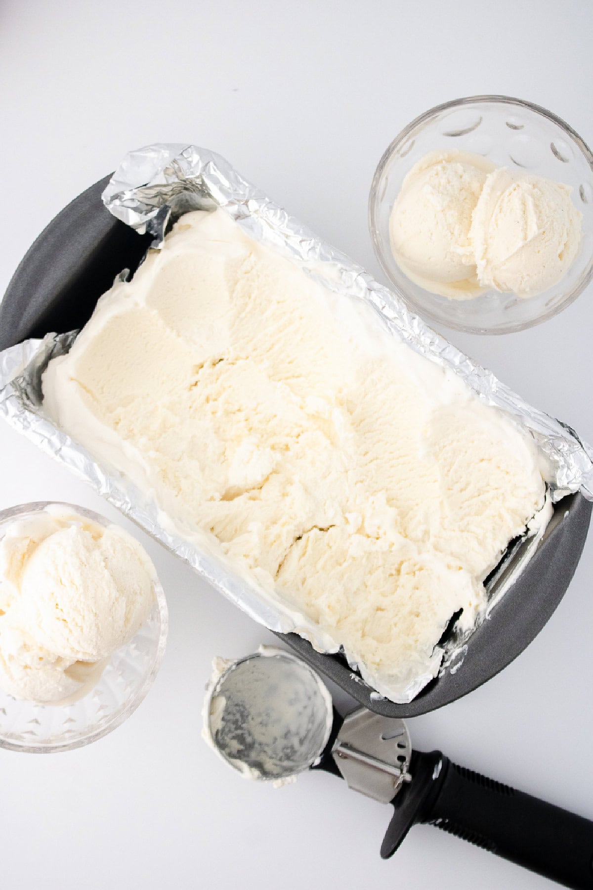 Homemade vanilla bean ice cream in a loaf pan with scoops served in glass bowls.