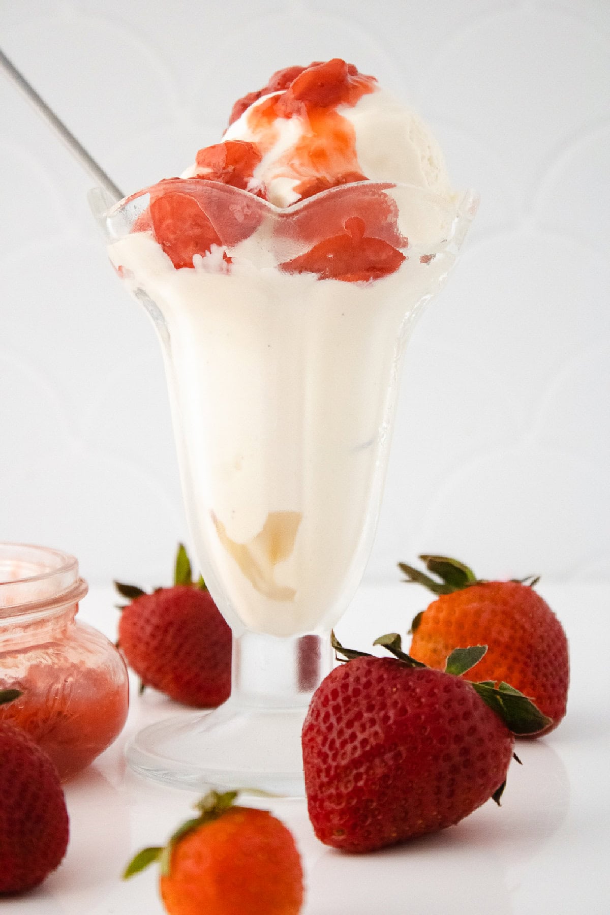 Vanilla bean ice cream sundae topped with strawberry sauce in a tall glass with fresh strawberries.