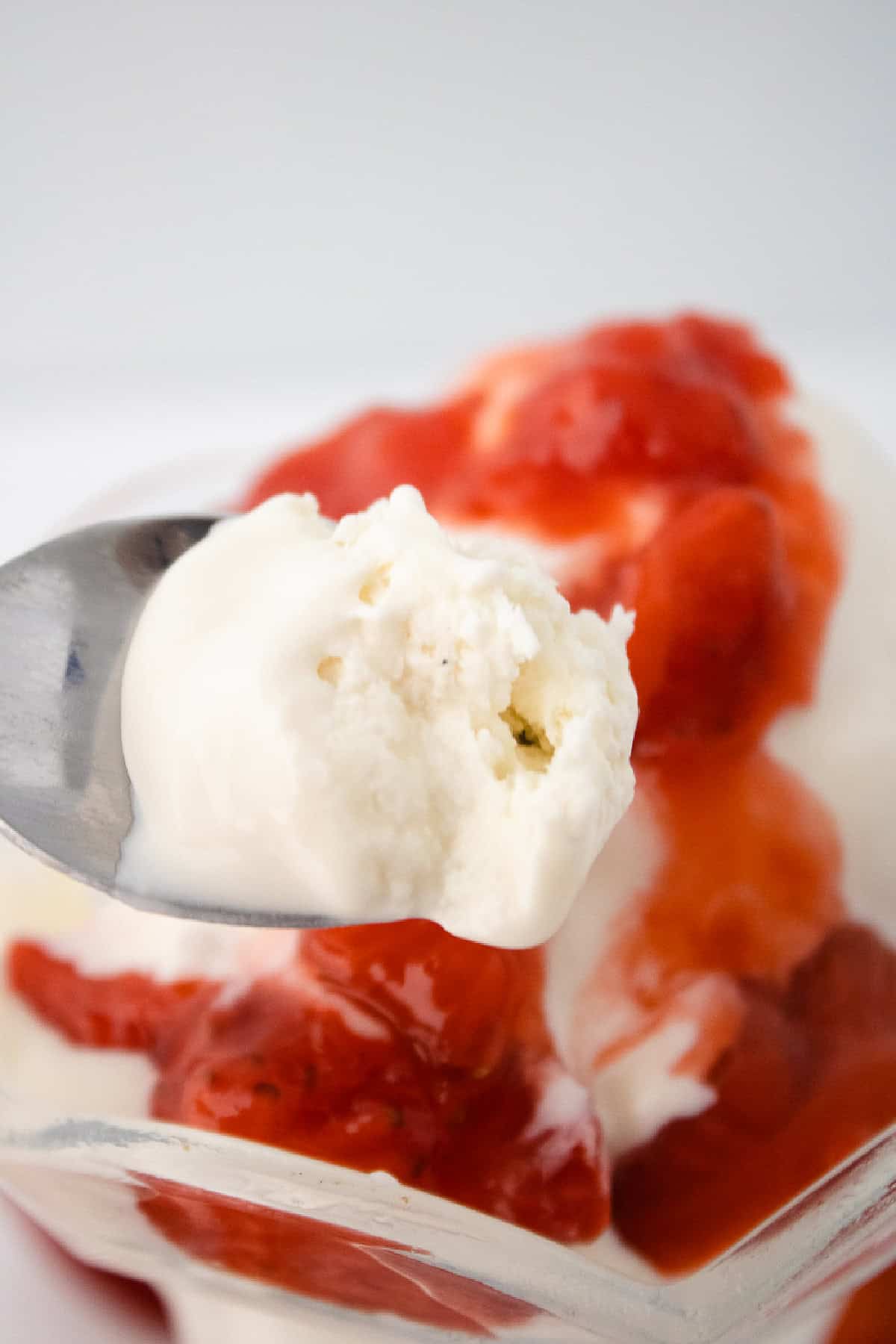 Spoonful of vanilla bean ice cream topped with fresh strawberry sauce.