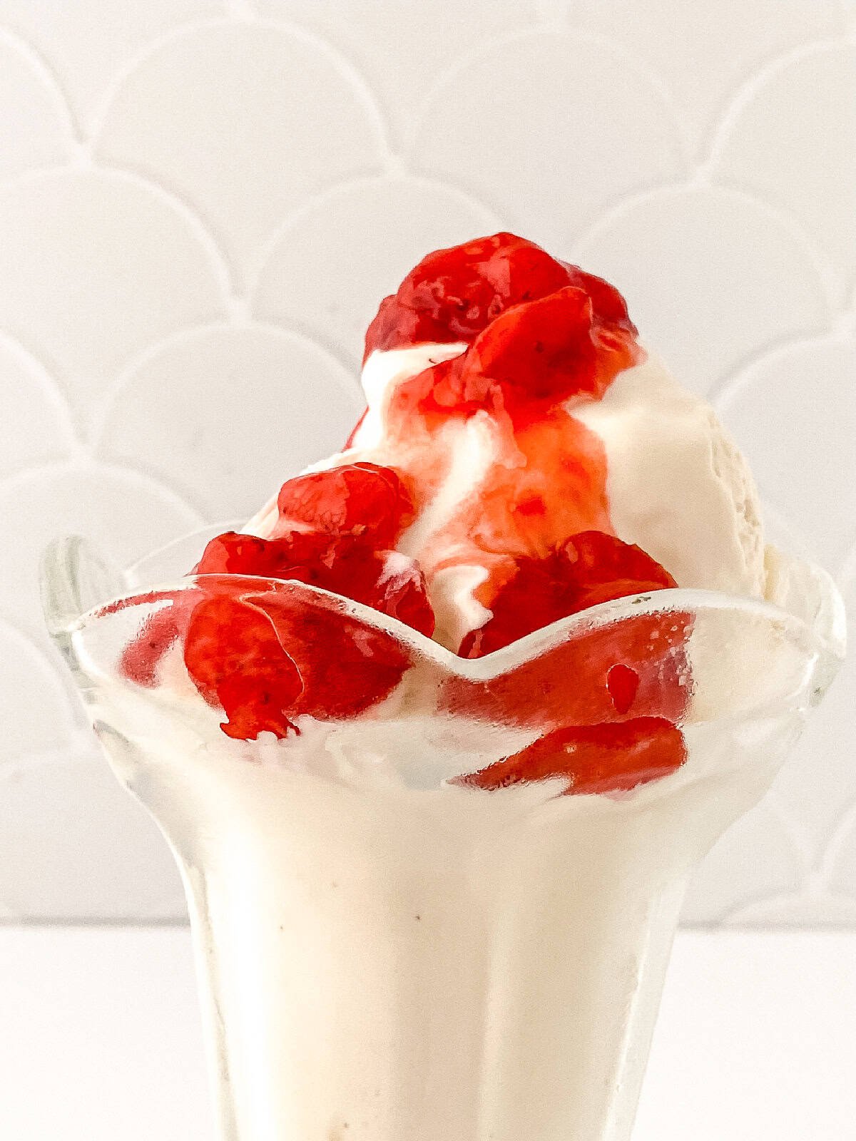 Close-up of vanilla bean ice cream sundae drizzled with strawberry topping in a glass dish.