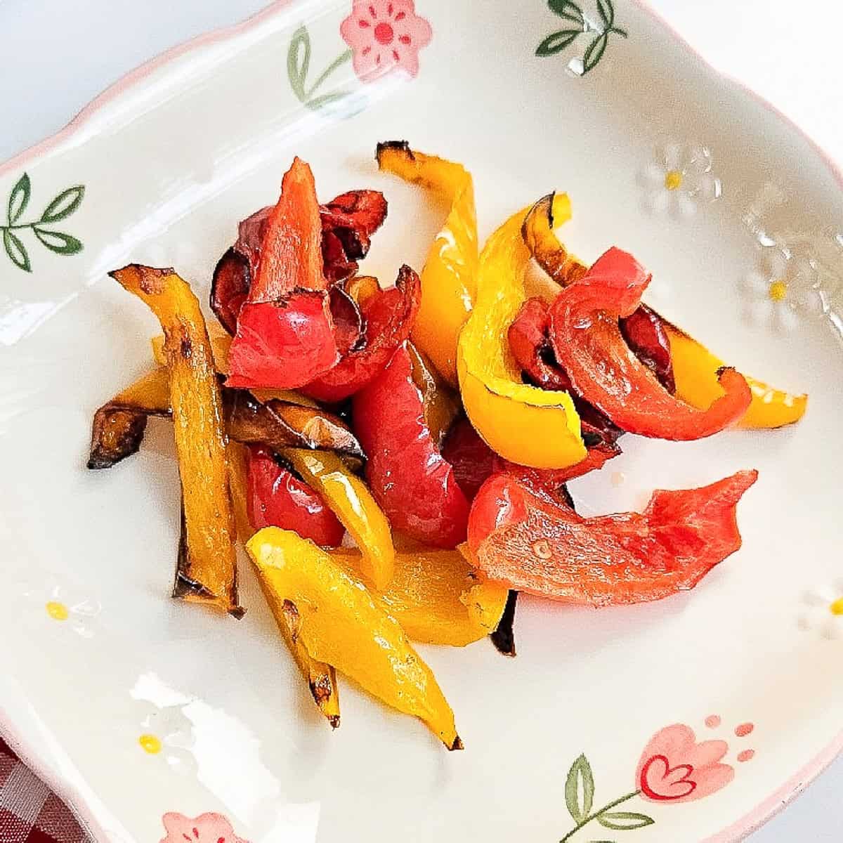 Colorful red and yellow peppers roasted in the air fryer, served on a white floral dish.