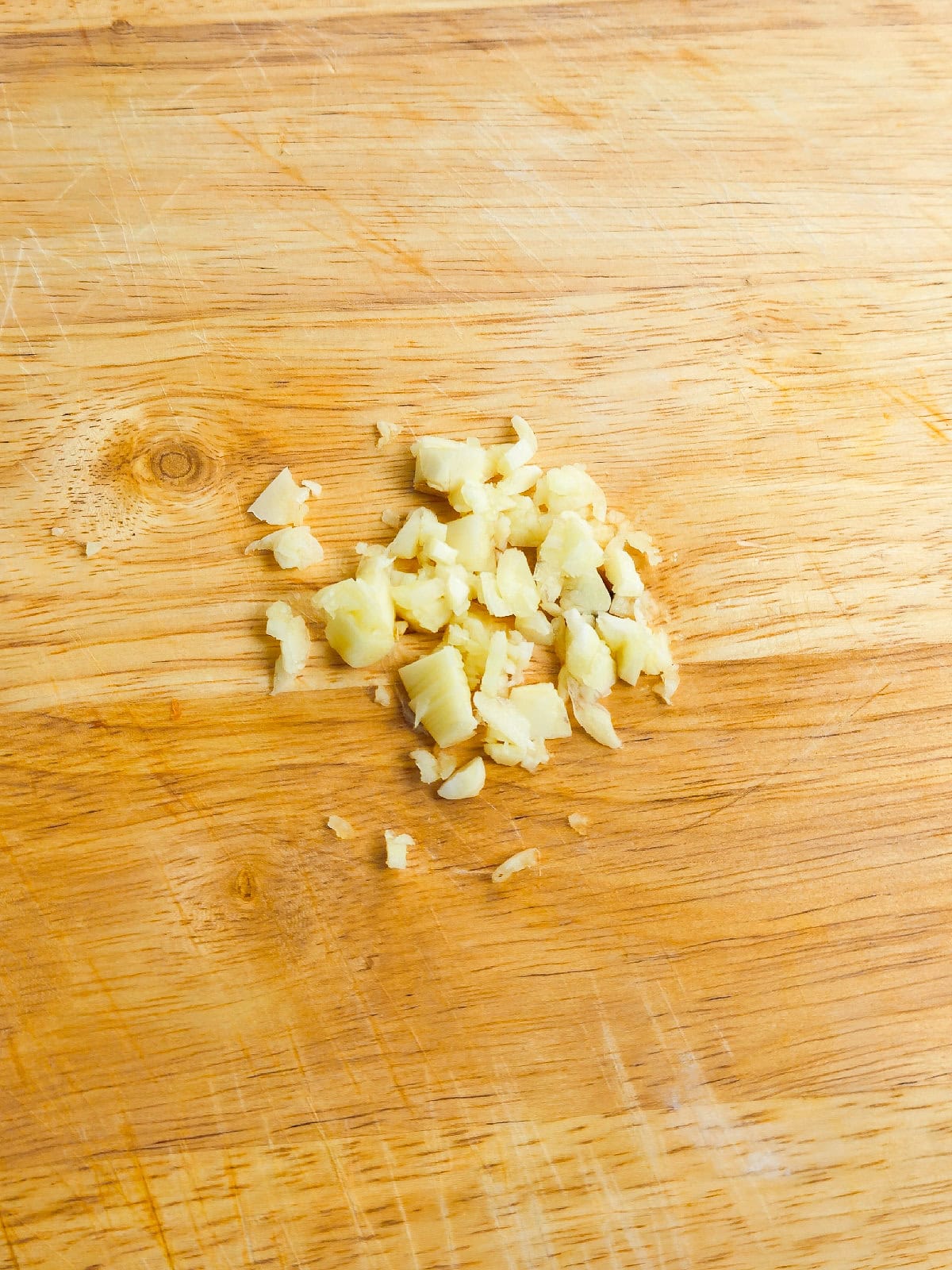 Minced fresh garlic cloves on a wooden cutting board for seasoning.
